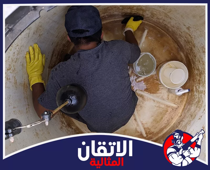 تنظيف المجالس من البقع والروائح بالأحساء 0567008659 شركة الإتقان المثالية عامل ينظف خزان مياه من الداخل بقفازات صفراء، ويمسح الجدران المتسخة بجوار دلاء وشعار الإتقان المثالية