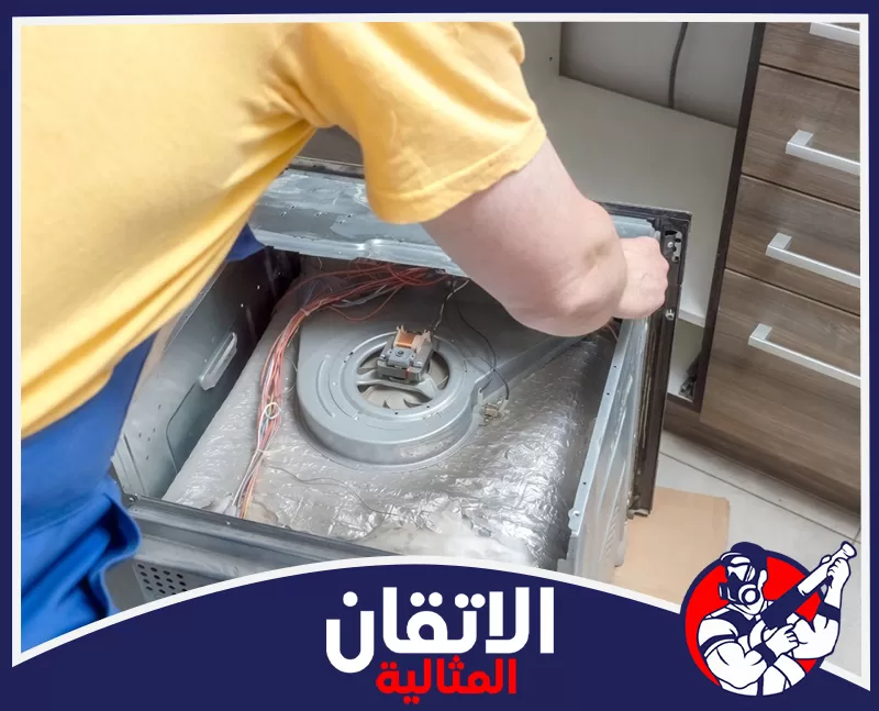 صيانة افران الغاز بالظهران بمركات مختلفة 0567008659 شركة الإتقان المثالية فني يفحص الأسلاك والتوصيلات الداخلية لفرن مفتوح من الخلف، أثناء صيانة الأفران بشركة الإتقان المثالية