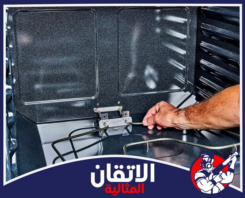 شركة تنظيف افران بالظهران 0567008659 شركة الإتقان المثالية فني من شركة الإتقان المثالية يفحص عنصر التسخين داخل فرن كهربائي مفتوح باستخدام أداة صيانة معدنية.